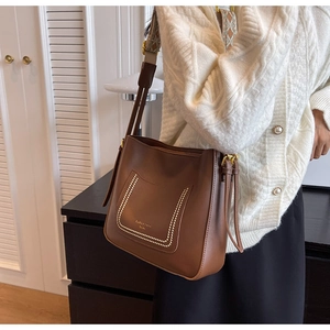 Detail of dark brown leather bucket bag featuring a jacquard woven wide shoulder strap