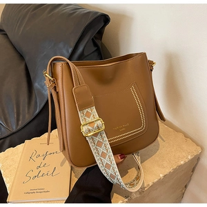 Close-up of brown leather bucket bag with retro geometric jacquard strap and gold hardware