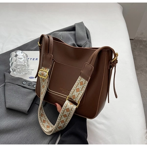 Detail of dark brown leather bucket bag with jacquard woven strap and gold buckle
