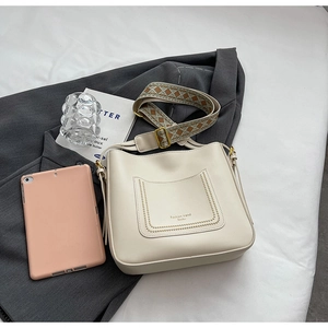 Close-up of beige bucket bag featuring a patterned strap and decorative front pocket