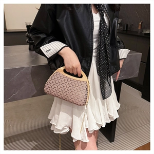Fashionable woven clutch bag with bamboo top handle and gold chain strap on a model