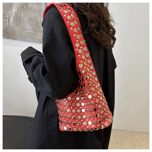 Détail du sac à bandoulière en cuir rouge avec rivets métalliques sur trench-coat noir