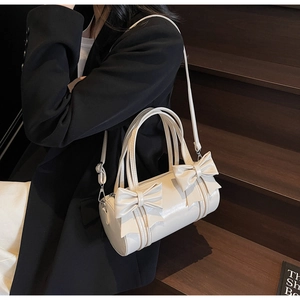 Detail of cream white cylinder crossbody bag with elegant bow accents on a leather finish