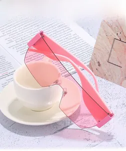 Pink oversized one-piece frameless sunglasses displayed on a white coffee cup