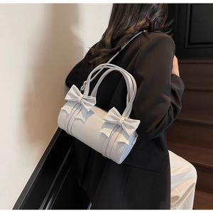 Close-up of light gray cylinder handbag featuring decorative bows and double handles