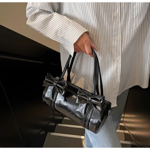Close-up of black cylinder handbag showing shiny patent leather and large bow details