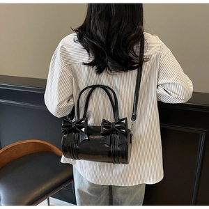 Detailed back view of a black glossy bow-knot cylinder bag on a model shoulder