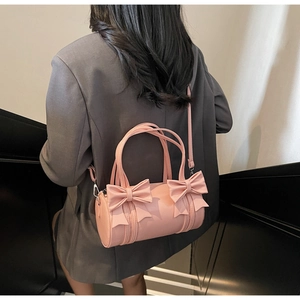Model wearing a pink cylindrical bow handbag with a crossbody strap over a grey blazer