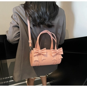 Detailed back view of pink cylindrical bow handbag worn over a grey blazer