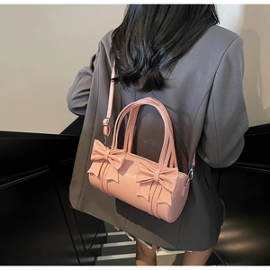 Detail of pink cylindrical barrel bag featuring large bows and glossy patent leather finish