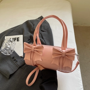Pink cylinder bow handbag with shoulder strap placed on a white bed and grey blazer