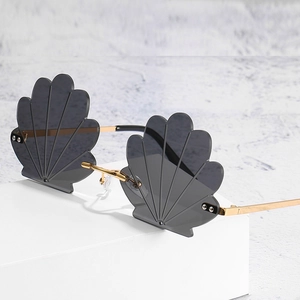 Frameless shell-shaped sunglasses with dark lenses and gold metal frame on a white block