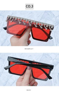 Detail of square oversized sunglasses featuring sparkling rhinestone tassels and red lenses