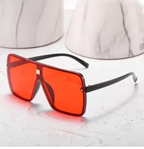 Detail of oversized square sunglasses with red lenses and gold metal studs on marble
