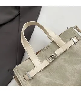 Detail of beige canvas tote bag showing leather handles and silver twist lock closure