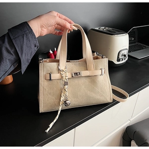 Detail of beige suede tote bag featuring silver twist lock and woven rope pendant