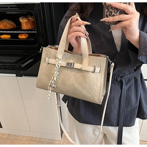 Detail of a beige tote bag featuring a leather strap closure and decorative rope charm