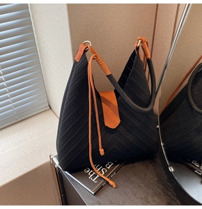 Detail of black woven tote bag with contrast orange knot handle on wooden background