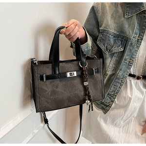 Close-up of contrast stitching tote bag with silver buckle and braided bell charm detail