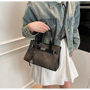 Detail of a charcoal gray tote bag with leather handles and metallic ball charm accessory