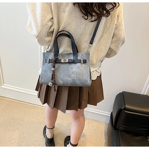 Detail of grey-blue leather handbag showing silver twist lock and woven charm pendant