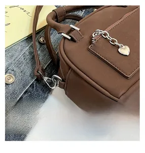 Close-up of brown PU leather pillow bag featuring silver zipper and heart pendant detail
