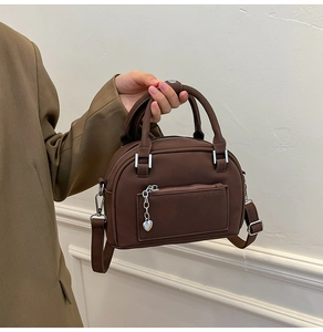 Detail of dark brown leather handbag featuring silver heart charm and front pocket