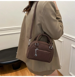 Detail of a brown leather pillow bag featuring a heart pendant and functional front zipper