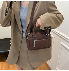 Detail view of brown crossbody pillow bag with silver chain and heart charm decoration