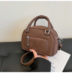 Detail of coffee brown pillow bag with matte faux leather, front zipper, and heart charm
