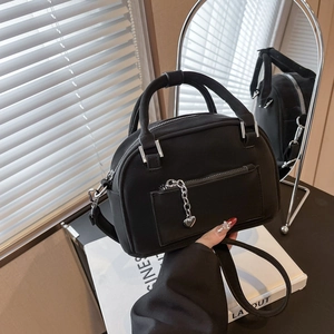 Black Boston style handbag with heart charm and crossbody strap under natural light