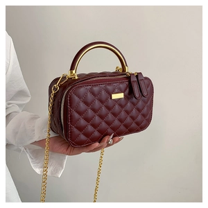 Close-up of wine red quilted leather bag with golden metal handle and dual zippers