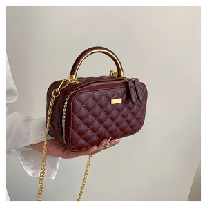 Detail of wine red quilted leather handbag with gold metal handle and chain strap