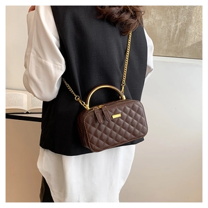 Detail of dark brown quilted crossbody bag with gold handle shown on a model