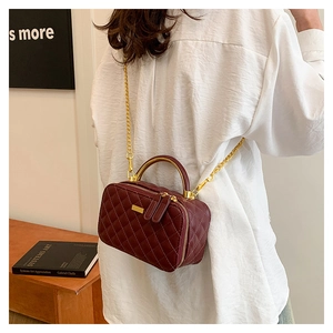 Detail of burgundy quilted leather handbag with gold chain strap and metal handle