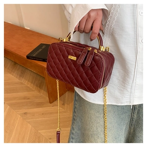 Detail of burgundy quilted crossbody bag with gold chain strap and metal handle