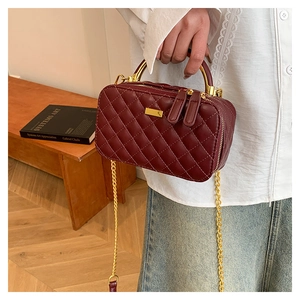 Detail of burgundy quilted crossbody bag with golden metal handle and chain strap
