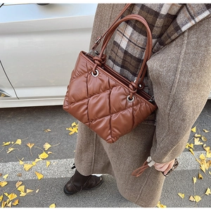 Close-up of brown quilted puffer tote bag with glossy finish and metal eyelet handles