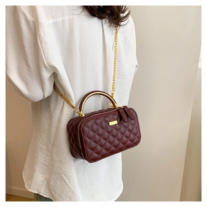 Close-up of wine red quilted crossbody bag with gold metal handle and chain strap