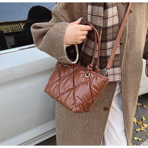 Close-up of brown quilted tote bag with diamond pattern held by model in autumn street