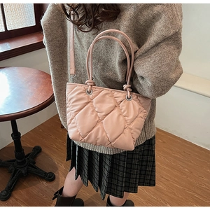 Pink quilted tote bag with large diamond stitch pattern worn as a crossbody shoulder bag
