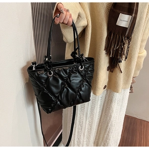 Detail view of black quilted puff handbag featuring textured rhombic pattern and top handles