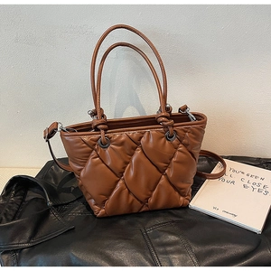 Detail of brown quilted puffer tote bag with glossy finish and cylindrical handles on leather