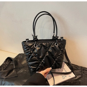 Detail of black quilted puffer tote bag with glossy finish on a stylish leather background