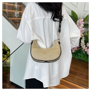 Detail shot of a beige woven crescent bag with black contrast piping and gold buckle
