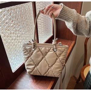 Detail of beige quilted tote bag showing rhombus texture and silver metal rings