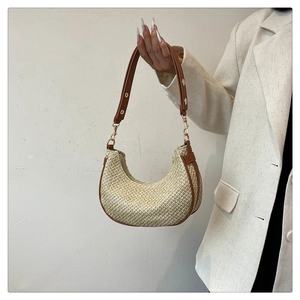 Detail of straw crescent bag featuring brown leather trim and golden metal rivets
