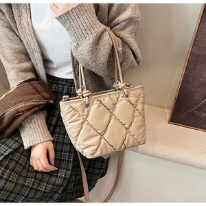 Detail of beige quilted puffer bag with soft texture and metallic strap rings
