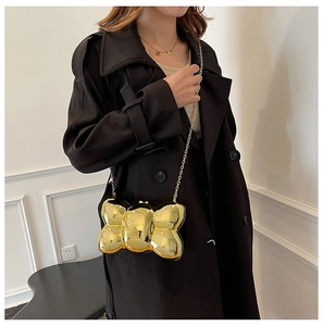 Elegante borsa da sera in acrilico dorato con catena indossata su un trench nero