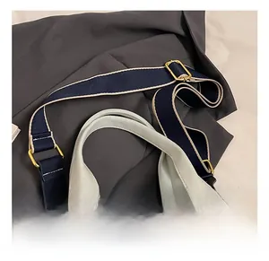 Detail of grey tote bag handles and adjustable navy strap with gold metal buckle